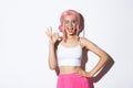 Beautiful cheeky girl in halloween costume and pink wig, showing okay sign in approval and winking, assure or recommend