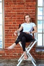 Beautiful cheeky young girl is sitting in a chair by the brick wall. Background brick brick, copy space