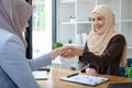 A beautiful and cheerful Asian Muslim businesswoman shaking hands with a female business partner during the meeting in Royalty Free Stock Photo