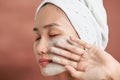 Beautiful cheerful Asian teen girl applying facial clay mask. Beauty treatments, isolated on light background Royalty Free Stock Photo