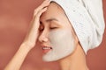 Beautiful cheerful Asian teen girl applying facial clay mask. Beauty treatments, isolated on light background Royalty Free Stock Photo