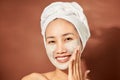 Beautiful cheerful Asian teen girl applying facial clay mask. Beauty treatments,  on light background Royalty Free Stock Photo