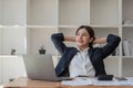 Beautiful and cheerful asian young businesswoman relaxing and stretching her arms and neck after work at her office desk Royalty Free Stock Photo