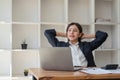 Beautiful and cheerful asian young businesswoman relaxing and stretching her arms and neck after work at her office desk Royalty Free Stock Photo