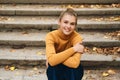 Beautiful cheerful casual girl happily looking in camera sitting on stairs in city park