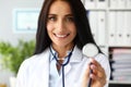 Beautiful cheerful female GP holding in hand stethoscope head