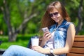 Beautiful cheerful girl with a smartphone sitting in a park on a bench on a sunny dayteenager, on-line shopping concept Royalty Free Stock Photo