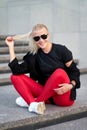 Portrait of young positive sporty woman wearing black sportswear, red leggings and trendy white sneakers. Outdoor shot on grey Royalty Free Stock Photo