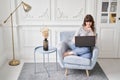 Beautiful cheerful girl using black laptop while sitting on sofa in living room at home. Young casual woman using laptop Royalty Free Stock Photo