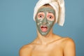 Beautiful cheerful teen girl applying facial clay mask. Beauty treatments,  on blue background Royalty Free Stock Photo