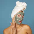 Beautiful cheerful teen girl applying facial clay mask. Beauty treatments,  on blue background Royalty Free Stock Photo