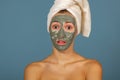 Beautiful cheerful teen girl applying facial clay mask. Beauty treatments,  on blue background Royalty Free Stock Photo