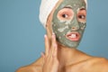 Beautiful cheerful teen girl applying facial clay mask. Beauty treatments, isolated on blue background Royalty Free Stock Photo