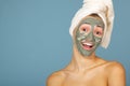 Beautiful cheerful teen girl applying facial clay mask. Beauty treatments, isolated on blue Royalty Free Stock Photo