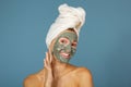 Beautiful cheerful teen girl applying facial clay mask. Beauty treatments, isolated over blue Royalty Free Stock Photo