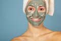 Beautiful cheerful teen girl applying facial clay mask. Beauty treatments, isolated on blue background Royalty Free Stock Photo