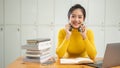 A beautiful Asian female student sits at a table with her laptop and a stack of books on the table Royalty Free Stock Photo