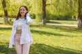 Beautiful cheerful young brunette woman standing in green park and smiling to camera. Royalty Free Stock Photo