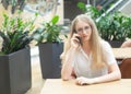 Portrait of a cheerful young caucasian blond business woman sitting on the table, talking at phone and looking at camera. Concept Royalty Free Stock Photo