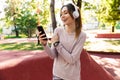 Beautiful cheerful young fitness sports woman posing outdoors in park listening music with earphones using mobile phone Royalty Free Stock Photo