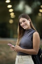 Beautiful cheerful young lady looking at camera texting and standing outside. Joyful blond woman staring at camera in Royalty Free Stock Photo