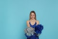 Beautiful cheerleader in costume holding pom poms on light blue background