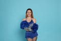 Beautiful cheerleader in costume holding pom poms on light blue background