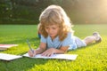 Beautiful child boy with book and pencil writing on notebook on grass background. Kids reading book in park. Royalty Free Stock Photo