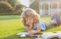 Beautiful child boy with book writing notes in copybook on grass background. Kids reading book in park.