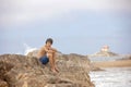 Beautiful child, boy, sitting on a big rock in the ocean, beach in Portugal on a cloudy foggy day Royalty Free Stock Photo