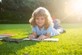 Beautiful child boy writing notes in copybook, laying on grass on the meadow background. Kids reading book in park. Royalty Free Stock Photo