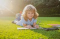 Beautiful child boy writing notes in copybook, laying on grass on the meadow background. Kids reading book in park. Royalty Free Stock Photo