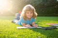 Beautiful child boy writing notes in copybook, laying on grass on the meadow background. Kids reading book in park. Royalty Free Stock Photo