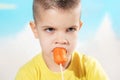 Beautiful child eats fresh carrot on a stick. Boy gnaws vegetables on a blue background Royalty Free Stock Photo