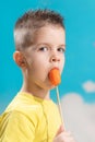 Beautiful child eats fresh carrot on a stick. Boy gnaws vegetables on a blue background Royalty Free Stock Photo
