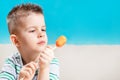 Beautiful child eats fresh carrot on a stick. Boy gnaws vegetables on a blue background Royalty Free Stock Photo