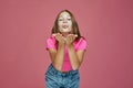 Beautiful child girl blowing kiss at camera, pretty schoolgirl sending air kisses on pink background. Love, gratefulness Royalty Free Stock Photo