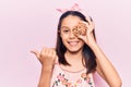 Beautiful child girl holding cookie pointing thumb up to the side smiling happy with open mouth Royalty Free Stock Photo