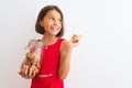 Beautiful child girl holding jar of cookies standing over isolated white background very happy pointing with hand and finger to Royalty Free Stock Photo