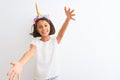 Beautiful child girl wearing unicorn diadem standing over isolated white background looking at the camera smiling with open arms Royalty Free Stock Photo