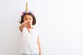 Beautiful child girl wearing unicorn diadem standing over isolated white background looking unhappy and angry showing rejection