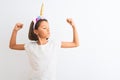 Beautiful child girl wearing unicorn diadem standing over isolated white background showing arms muscles smiling proud Royalty Free Stock Photo