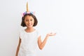 Beautiful child girl wearing unicorn diadem standing over isolated white background smiling cheerful presenting and pointing with Royalty Free Stock Photo