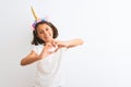 Beautiful child girl wearing unicorn diadem standing over isolated white background smiling in love doing heart symbol shape with Royalty Free Stock Photo