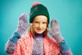 Beautiful child girl wears winter mittens, warm sweater, hat with pompom and openwork cape scarf on blue isolated