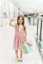 A beautiful child in the mall makes shopping. Online shopping concept. A girl in a pink dress with multi-colored pastel bags in
