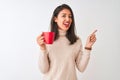 Beautiful chinese woman drinking red cup of coffee standing over isolated white background very happy pointing with hand and Royalty Free Stock Photo