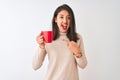 Beautiful chinese woman drinking red cup of coffee standing over isolated white background very happy pointing with hand and Royalty Free Stock Photo