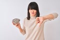 Beautiful chinese woman holding bowl with sunflowers seeds over isolated white background with angry face, negative sign showing Royalty Free Stock Photo