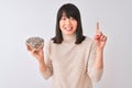 Beautiful chinese woman holding bowl with sunflowers seeds over isolated white background surprised with an idea or question Royalty Free Stock Photo